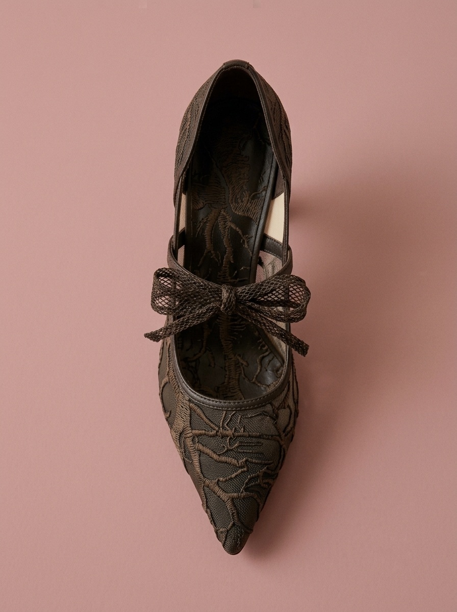 Top-down view of a dark brown lace high-heeled shoe featuring an embellished bow on a solid pinkish-brown studio background.