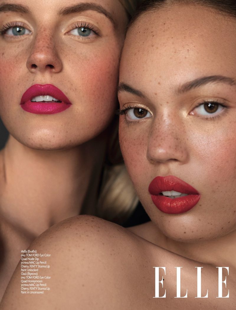 Close-up portrait of two adult women with freckles and bold lipstick in a beauty editorial for ELLE magazine, on a grey background.