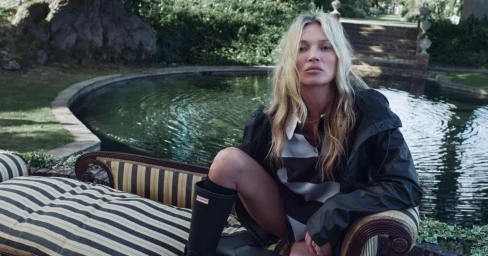 Model Kate Moss wearing black waterproof boots and jacket sitting outdoors by a pond for Hunter Iconic by Nature.
