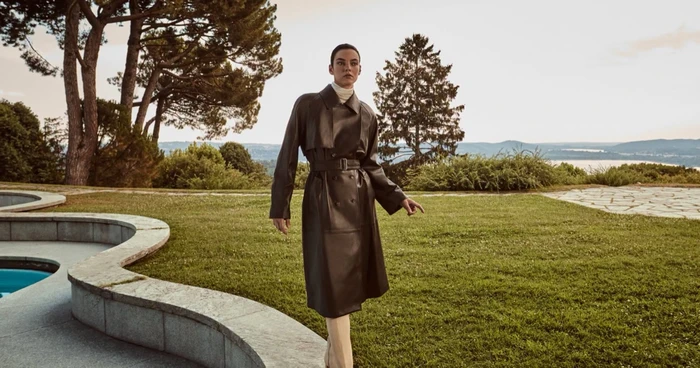 Model standing on a grassy lawn next to a curved pool wearing a dark leather trench coat for Vince