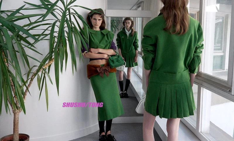 Models in green apparel posing in a hallway with mirrors and a large potted plant for Shushu/Tong A/W 26