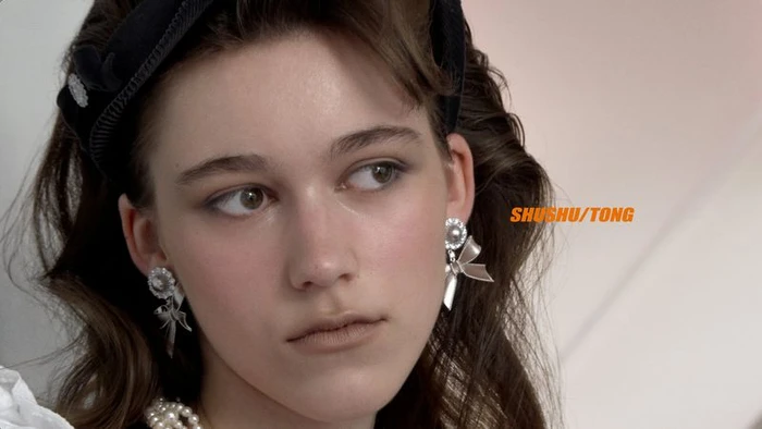 Close-up portrait of a female model wearing a black headband, pearl necklace, and ornate bow earrings for Shushu/Tong.