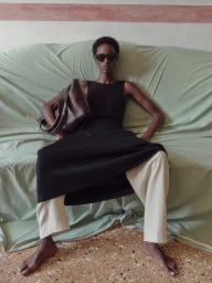 Model Bibi Abdulkadir seated on a green draped sofa holding a brown leather bag for RSVP Paris, photographed by Janne Rugland.