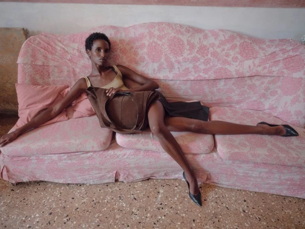 Model Bibi Abdulkadir reclining on a pink patterned sofa holding a brown leather bag, photographed by Janne Rugland