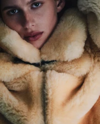 Close-up portrait of a model wearing a thick cream-colored shearling collar coat for the Helmut Lang campaign.