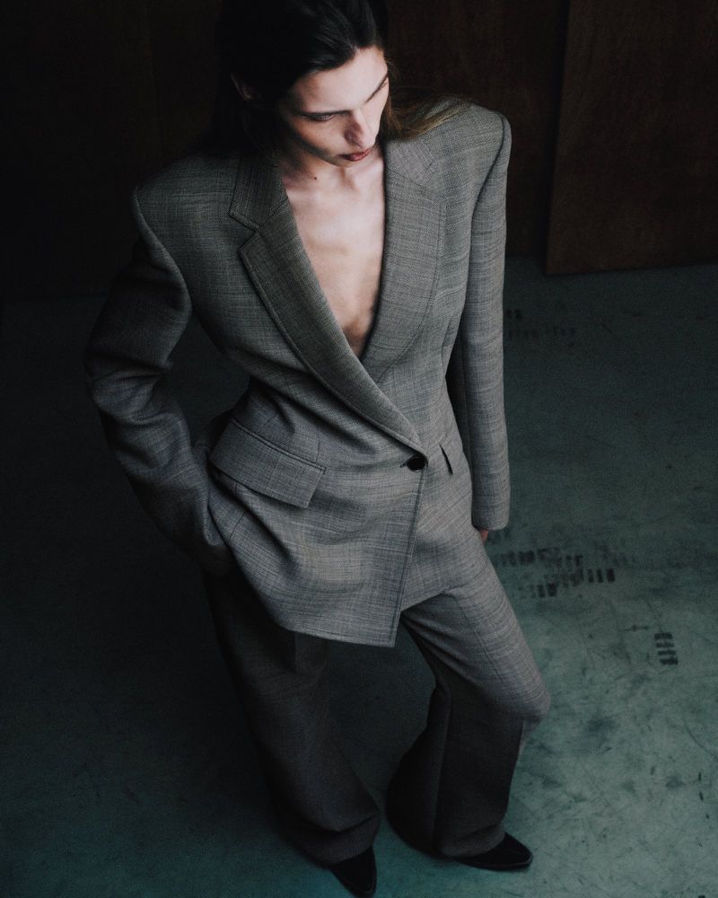 Model wearing a grey tailored pantsuit in a dimly lit industrial space shot from an elevated angle