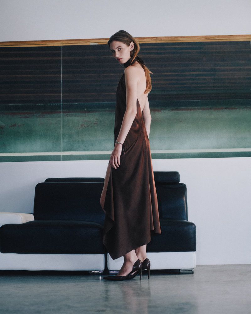 Model in a brown backless dress standing in front of a dark sofa and green wall panels for Helmut Lang.