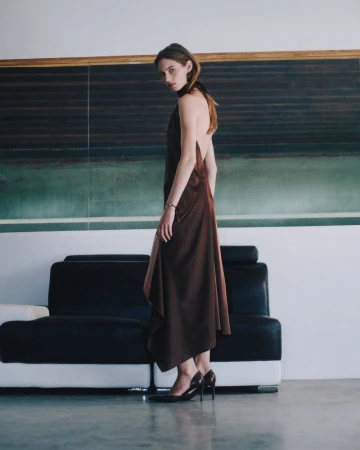 Model in a brown backless dress standing in front of a dark sofa and green wall panels for Helmut Lang.