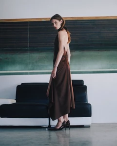 Model in a brown backless dress standing in front of a dark sofa and green wall panels for Helmut Lang.
