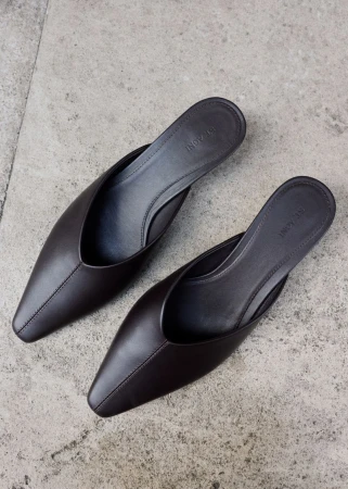 A pair of dark brown pointed-toe leather mules resting on a mottled grey stone surface from above