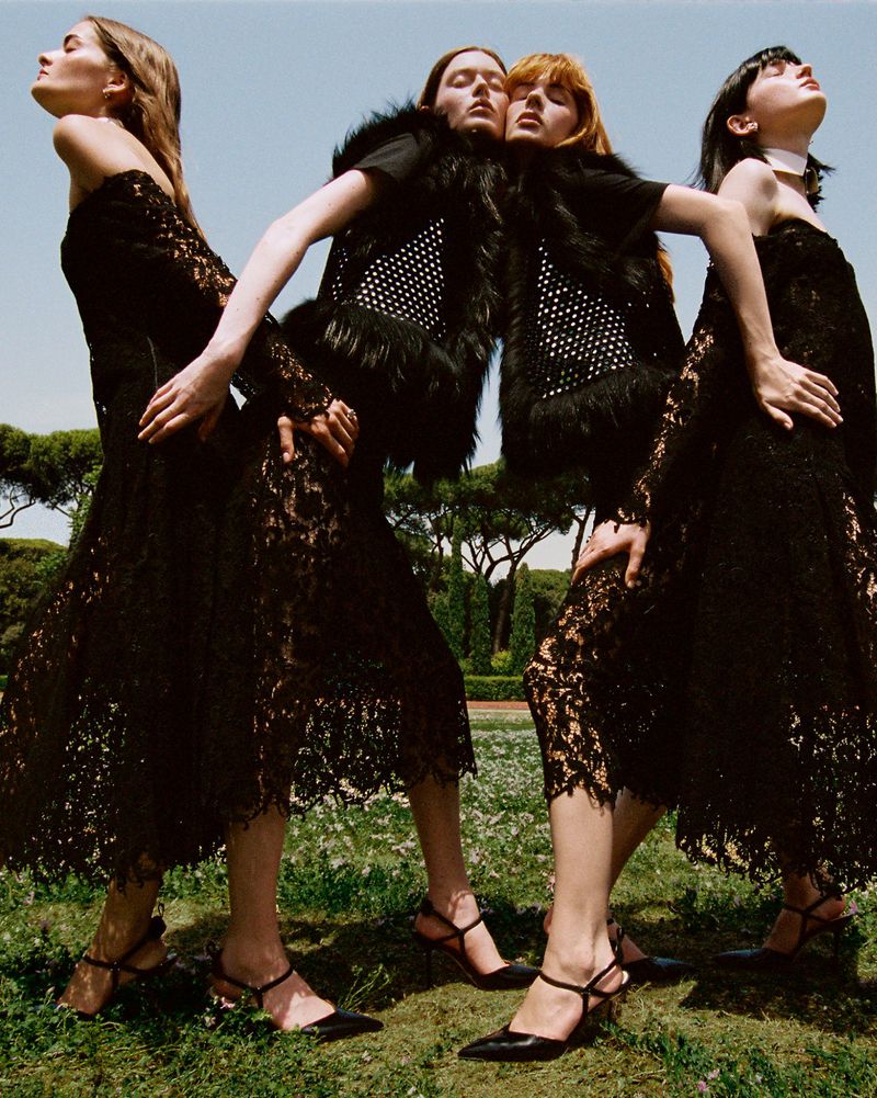 Four female models in black lace dresses posing outdoors against a park and bright blue sky background