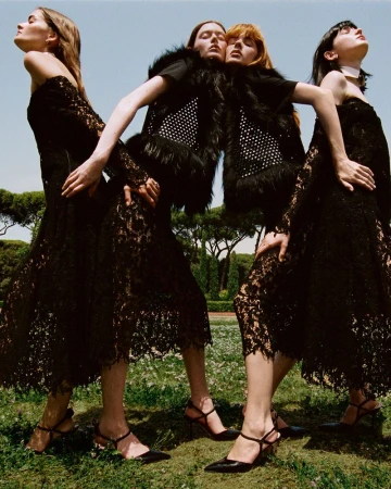 Four female models in black lace dresses posing outdoors against a park and bright blue sky background