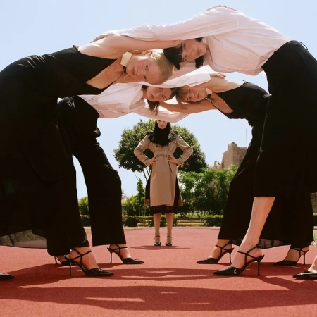 Four models forming a human arch overhead while another model stands framed in the center wearing a tan coat.