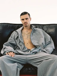 Romeo Beckham wearing a patterned grey jacket and trousers while seated on a black leather couch