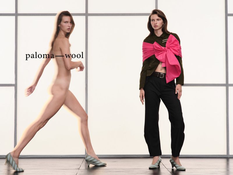 Two women posing against a grid studio backdrop for Paloma Wool, featuring one nude model walking and one dressed in dark trousers and green jacket.