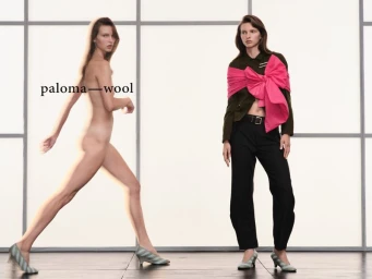 Two women posing against a grid studio backdrop for Paloma Wool, featuring one nude model walking and one dressed in dark trousers and green jacket.