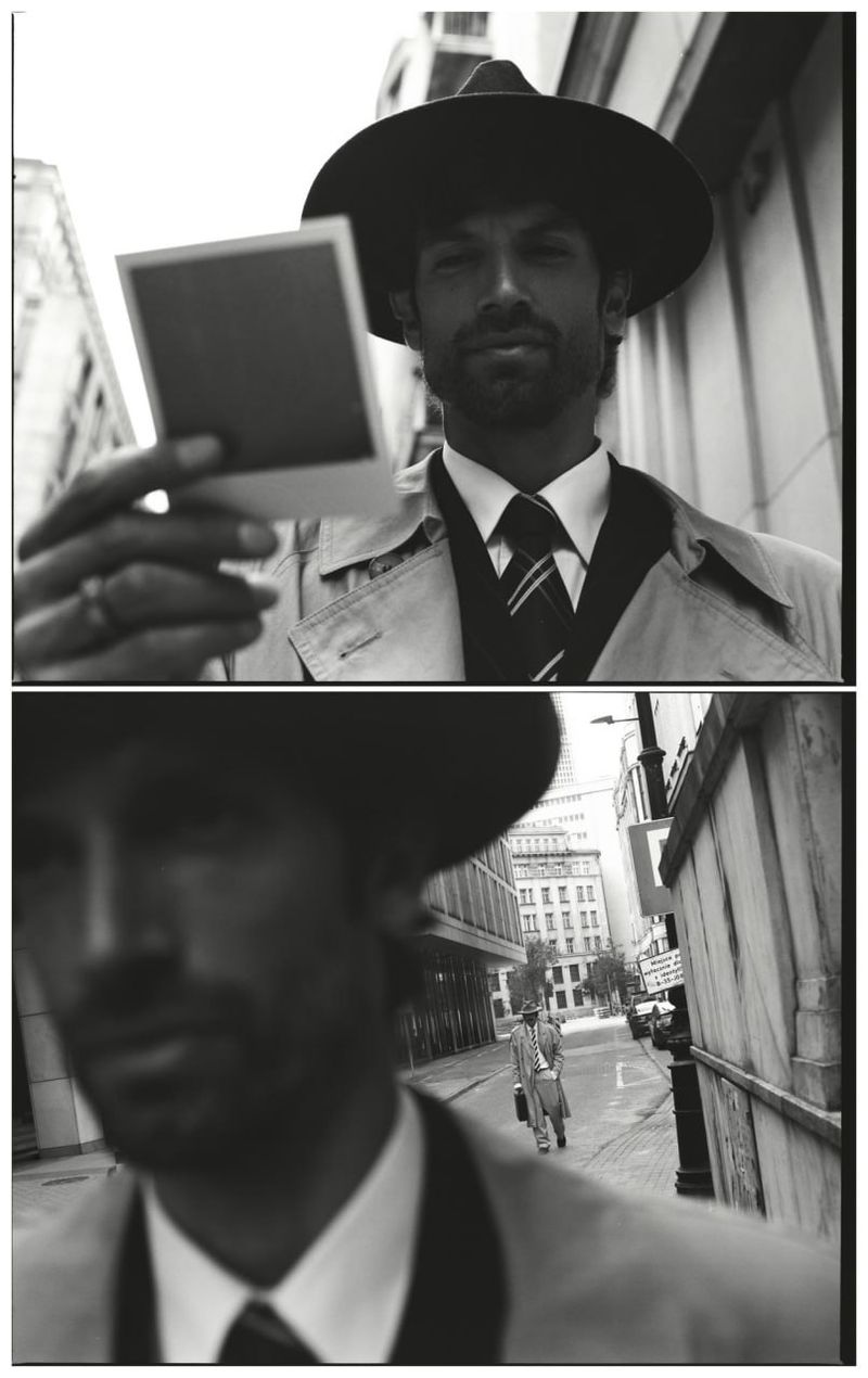 Man wearing a fedora hat and trench coat holding a polaroid photo outdoors in a split frame black and white editorial image.