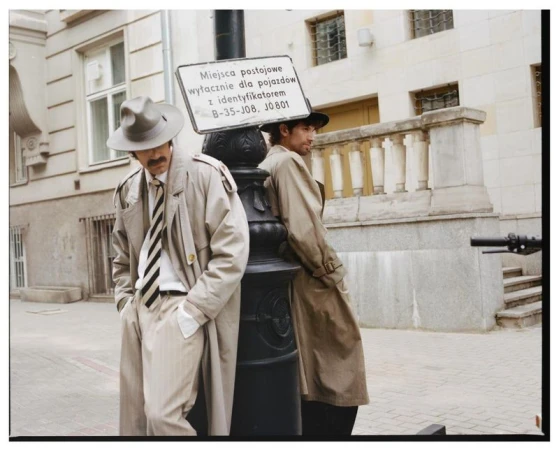 Two men in trench coats and fedora hats leaning against a lamppost on an urban street for Numero Netherlands.