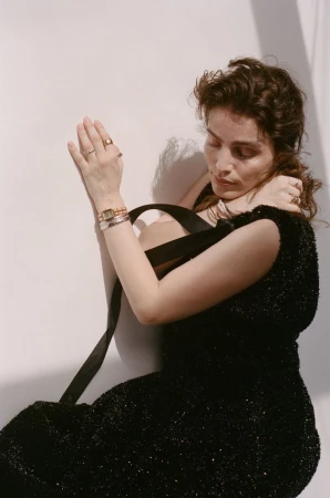 Lux Pascal wearing a textured black dress and luxury jewelry against a neutral wall for RUSSH x Chanel Accessories Special.