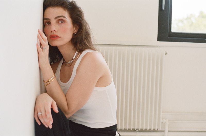Woman in white tank top leaning against a white wall next to a radiator for Russh