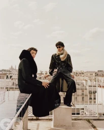 Two male models in dark outerwear seated on a rooftop overlooking a city skyline for GQ Middle East editorial