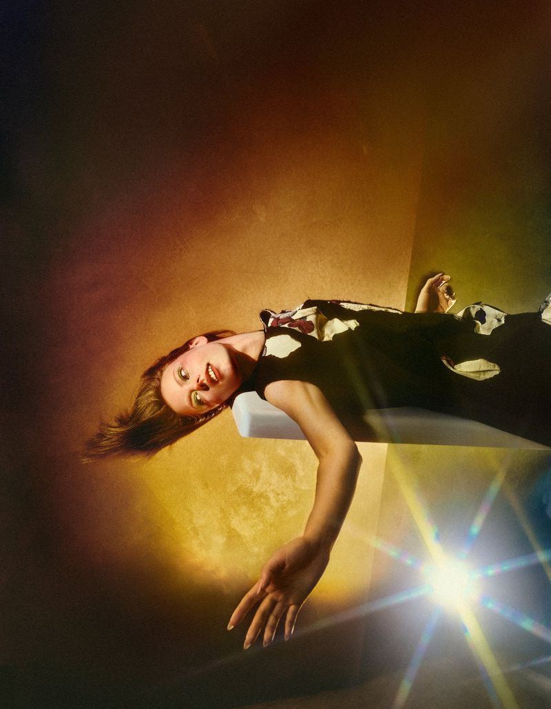 Model Karyna Maziar in a patterned top reclining horizontally under warm colored lighting with lens flare for T Magazine Germany