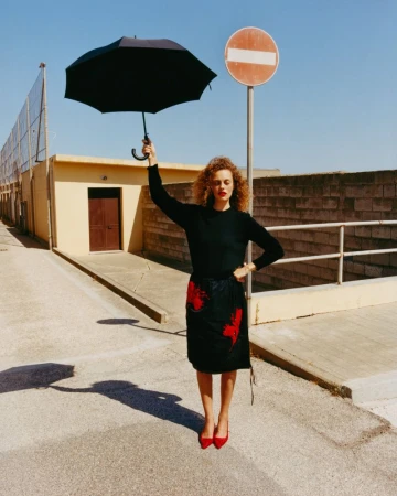 Model Gemma Janes holding a black umbrella under a clear blue sky for iO Donna