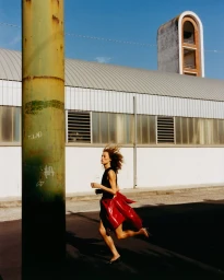 Model Gemma Janes running outdoors past an industrial building wearing a dark top and tied red jacket for iO Donna