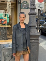 Model standing on a Paris street next to a Rue de la Paix sign wearing a dark blazer and fur-hem skirt.