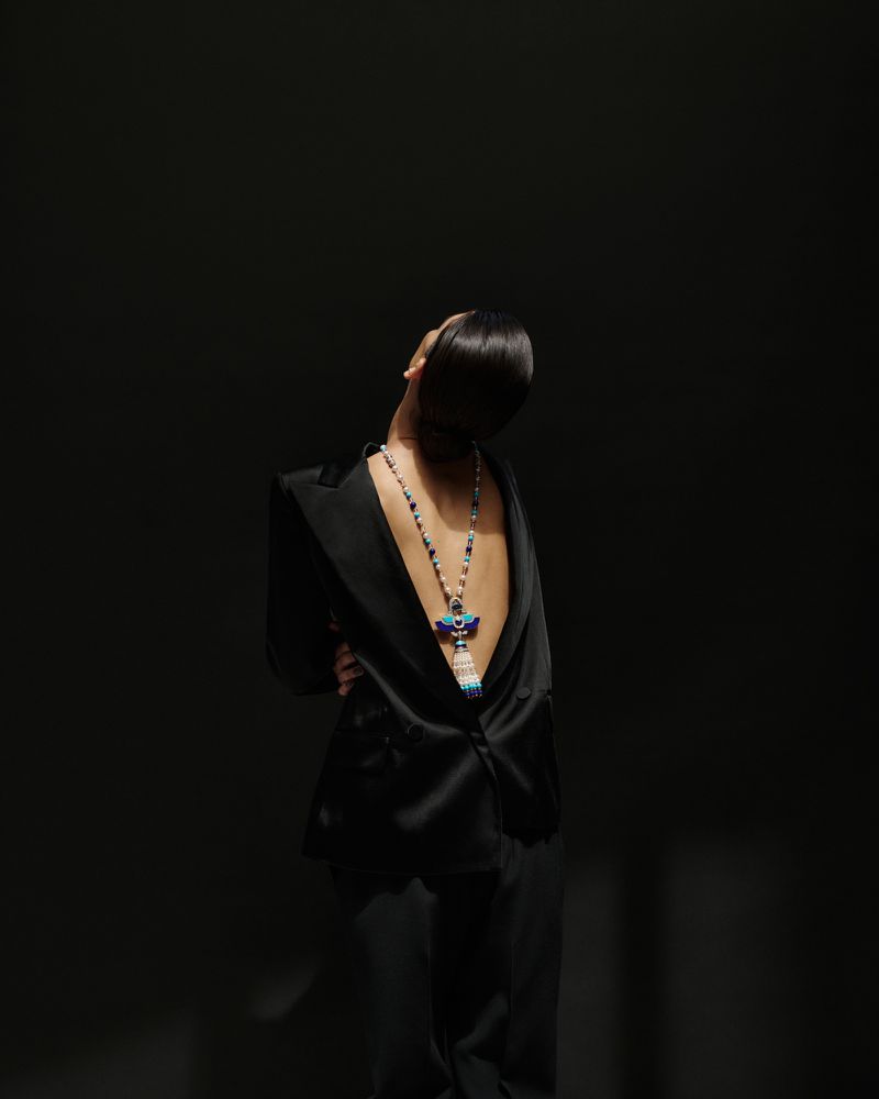 Model wearing a black suit jacket backwards with a beaded statement necklace along the bare back