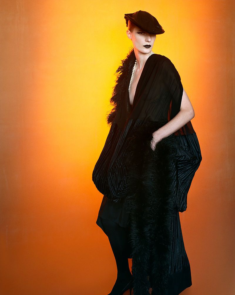 Model Julia Nobis wearing a black dress and feathered hat against an orange gradient backdrop for W Magazine