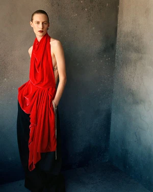 Model Julia Nobis wearing a draped red halter top and black trousers against a textured grey concrete wall for W Magazine.