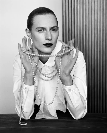Model Julia Nobis wearing a white buttoned shirt and draping long strands of pearl necklaces across her hands for W Magazine