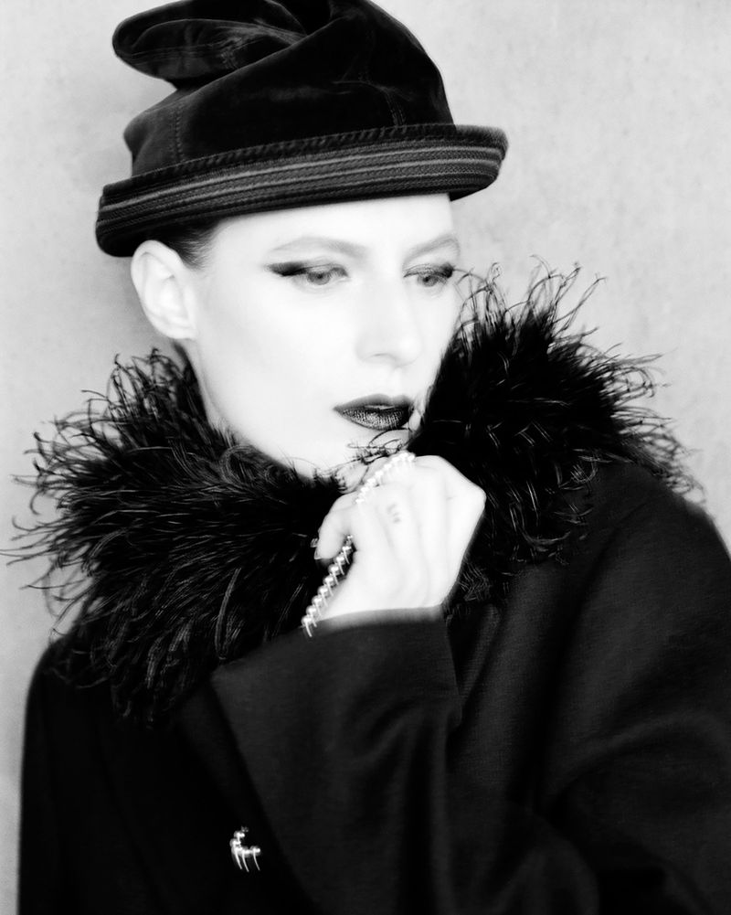 Model Julia Nobis wearing a dark hat and feather-trimmed coat for W Magazine photographed by Alasdair McLellan