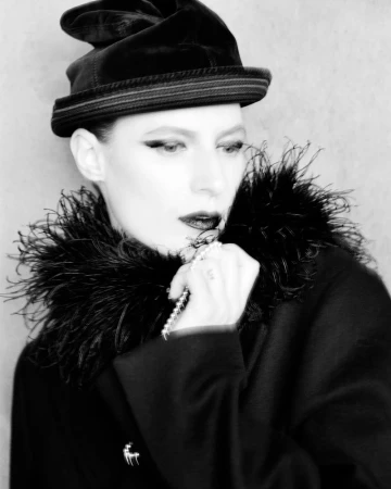 Model Julia Nobis wearing a dark hat and feather-trimmed coat for W Magazine photographed by Alasdair McLellan
