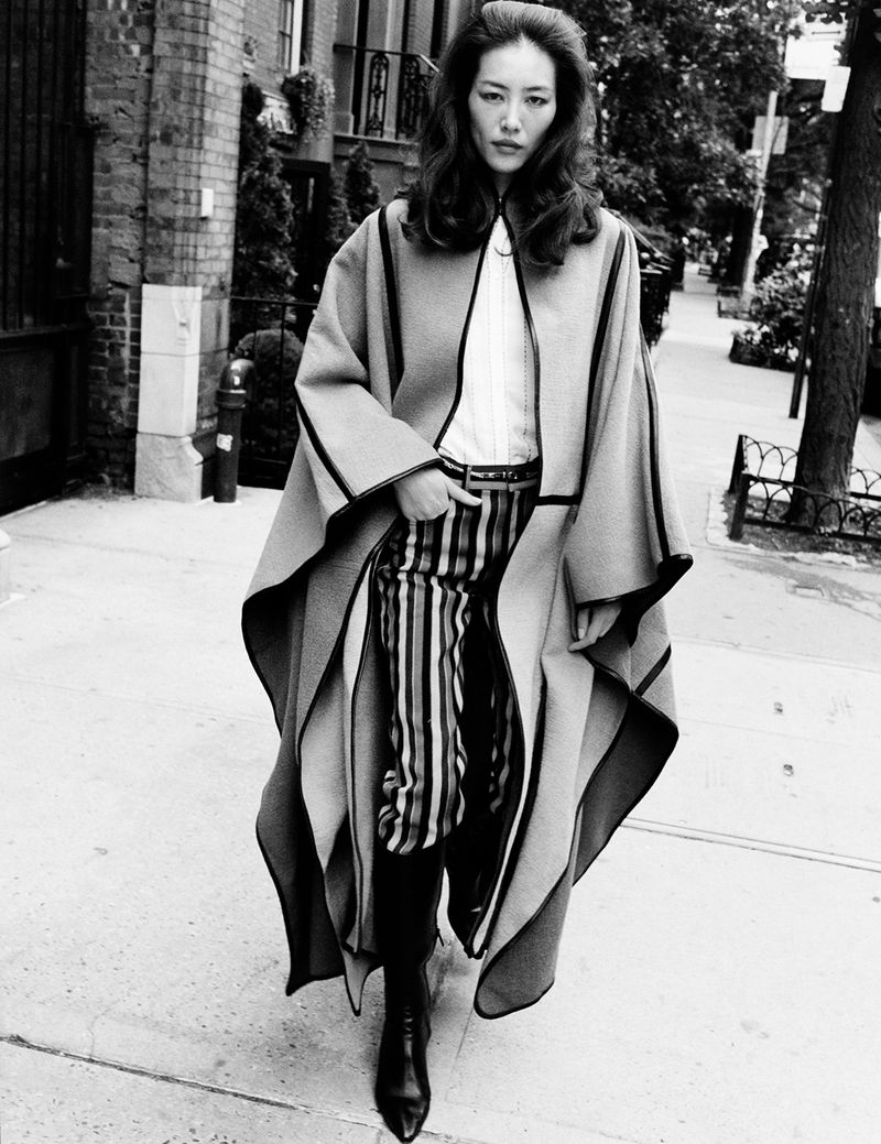 Model Liu Wen walking on a city sidewalk wearing a long poncho and striped pants, photographed by Angelo Pennetta.