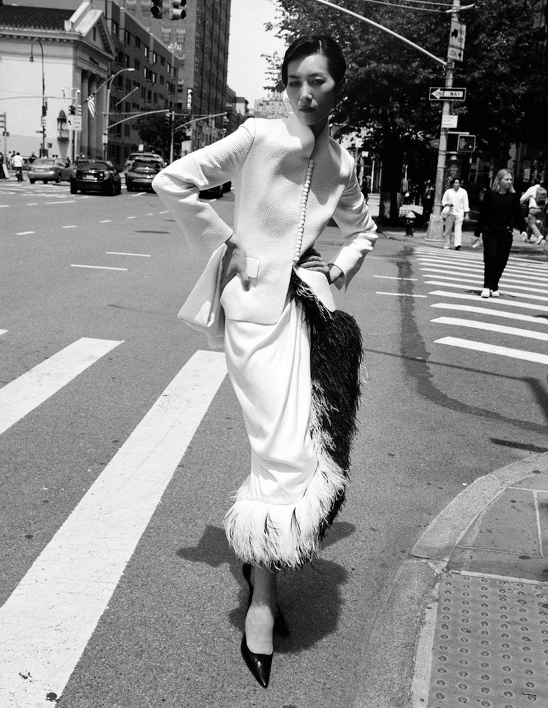 Model Liu Wen standing on a city street wearing a structured white jacket and feathered skirt for W Magazine