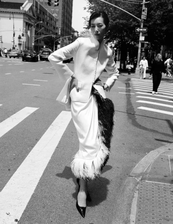 Model Liu Wen standing on a city street wearing a structured white jacket and feathered skirt for W Magazine