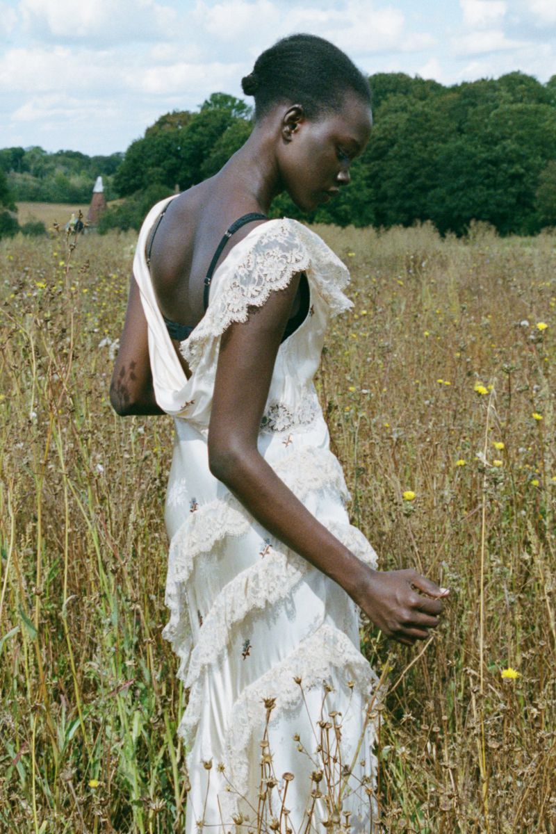 Model wearing a white lace-trimmed slip dress standing in a grassy meadow under a bright sky