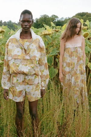 Two models standing in a sunlit field of tall grass and sunflowers for the Sea SS27 lookbook campaign.