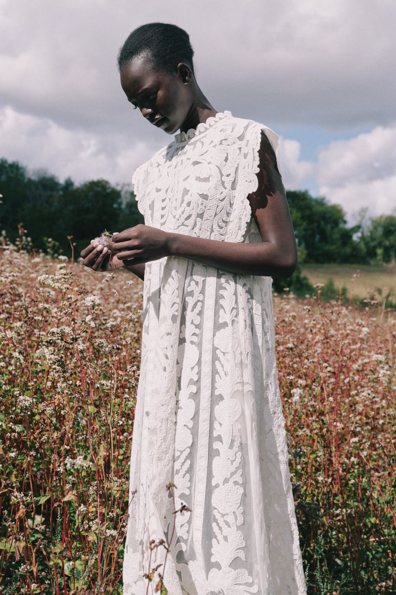 Model wearing a white lace dress standing in a wildflower field under an overcast sky for Sea lookbook