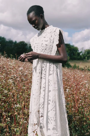 Model wearing a white lace dress standing in a wildflower field under an overcast sky for Sea lookbook