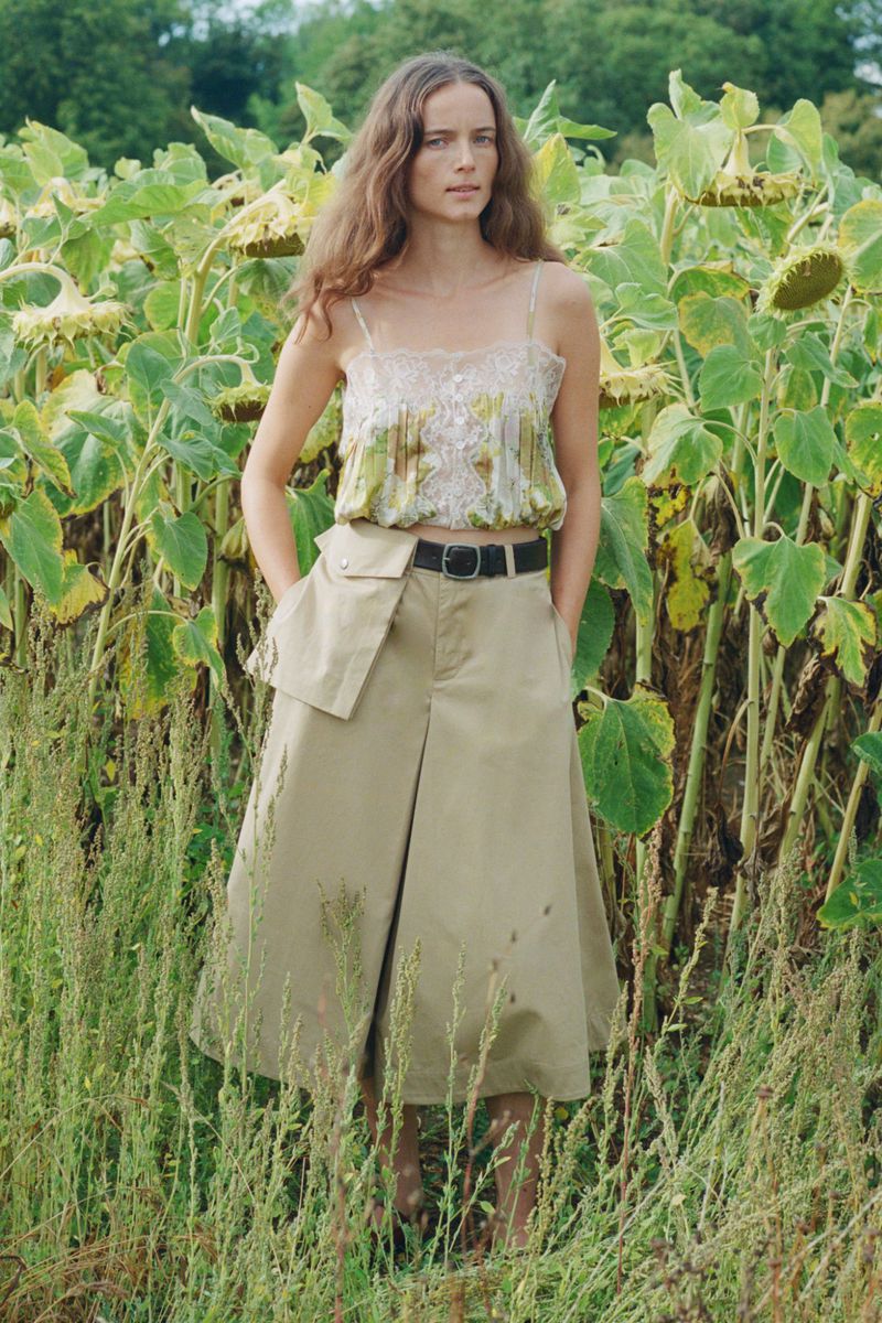 Model standing outdoors in a field of tall sunflowers wearing a patterned camisole and khaki midi skirt for Sea SS27 Lookbook.