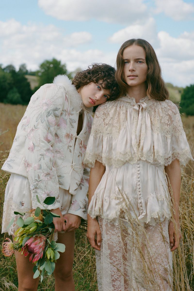 Two female models posing in a grassy meadow wearing cream-coloured embroidered and lace garments for Sea SS27 lookbook.