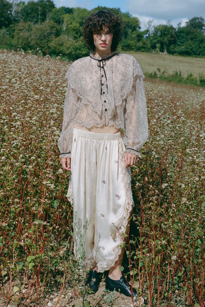 Model standing in a wild meadow wearing a sheer patterned blouse and light trousers for Sea SS27 Lookbook