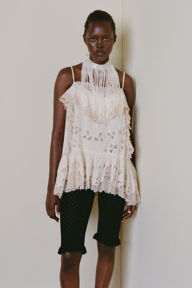 Model wearing a white fringe halter top and black patterned shorts against a plain neutral studio background