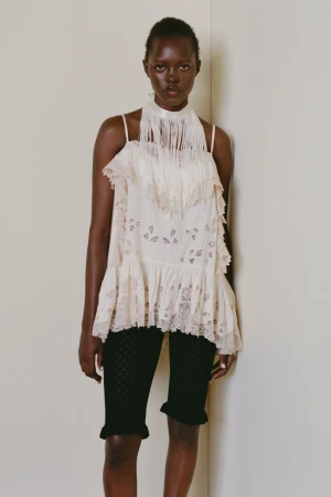Model wearing a white fringe halter top and black patterned shorts against a plain neutral studio background