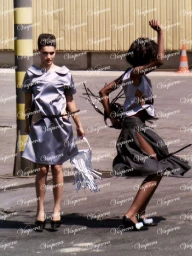 Two models in silver dresses outdoors on pavement with industrial background details, photographed by Dexter Lander.