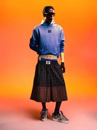 Model wearing a blue hoodie and plaid shorts against an orange gradient background