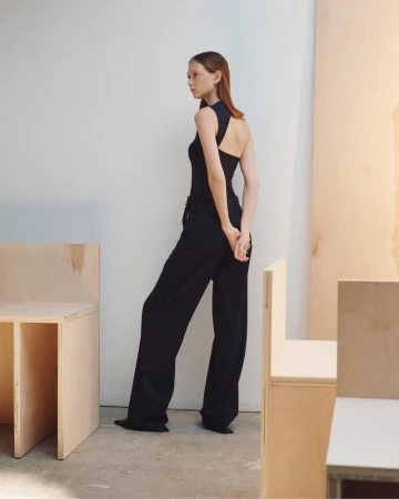 Model standing in a black top and trousers inside a minimalist studio with wooden partitions
